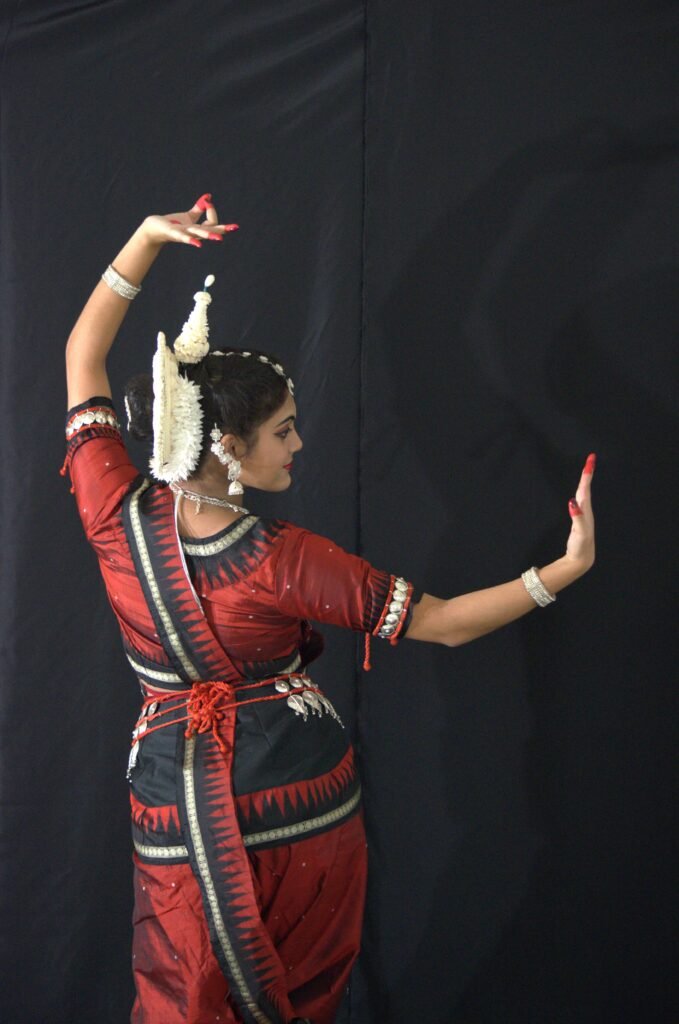 Odissi dancer standing in a graceful pose, adorned in traditional costume and makeup